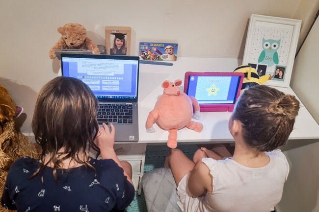 Six-year-old girl and four-year-old-girl work on their Reading Eggs lessons on iPad and laptop.